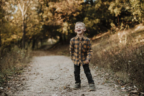 Cheerful boy looking away while standing on forest path stock photo