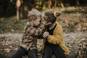 Bruder und Schwester sitzen sich im Herbst im Wald gegenüber - GMLF00894