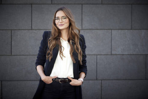 Confident business person with hands in pockets standing against brick wall - RHF02471