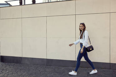 Geschäftsfrau mit Handtasche, die auf dem Gehweg gegen eine Mauer läuft - RHF02484