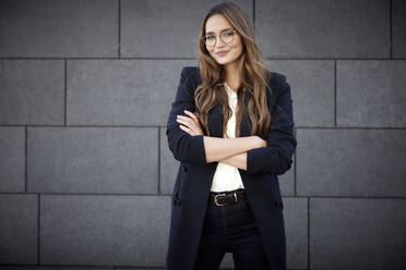 Young business professional standing with arms crossed against brick wall - RHF02493