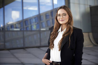 Confident businesswoman wearing eyeglasses with hand in pocket standing outdoors - RHF02498