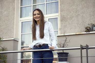 Junge Geschäftsfrau lächelt, während sie auf einem Balkon steht - RHF02505