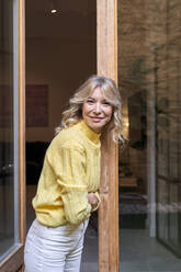 Smiling mature woman leaning on doorway at home - VEGF03261
