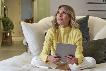 Modische reife Frau träumt, während sie ein digitales Tablet zu Hause hält - VEGF03271