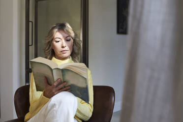 Ältere Frau im gelben Pullover liest zu Hause ein Buch - VEGF03278