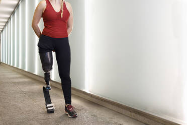 Sportswoman with prosthetic leg walking by wall in underpass - IFRF00160