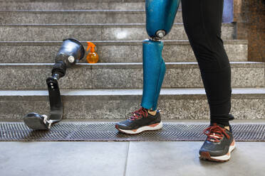 Young sportswoman with prosthetic leg standing by artificial limb on steps - IFRF00164