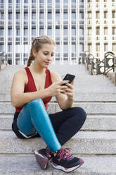 Sportlerin mit Beinprothese benutzt Mobiltelefon, während sie auf einer Treppe in der Stadt sitzt - IFRF00175