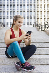 Sportswoman with prosthetic leg using mobile phone while sitting on steps in city - IFRF00175