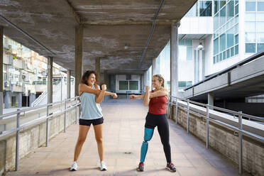 Sportswoman with prosthetic leg exercising with friend while standing on bridge - IFRF00177