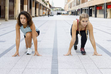 Sportlerinnen, die sich für ein Rennen auf einem Fußweg in der Stadt ducken - IFRF00183