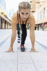 Junge Frau mit Beinprothese hockt beim Sportwettkampf auf dem Fußweg - IFRF00185