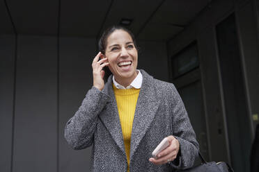 Businesswoman with mobile phone laughing while standing outdoors - SDAHF01028