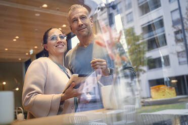 Confident business couple with digital tablet standing by window at modern cafe - SDAHF01041