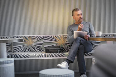 Thoughtful businessman with digital tablet looking away while sitting at cafe - SDAHF01043