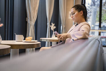 Geschäftsfrau, die ein Mobiltelefon benutzt, während sie in einem modernen Cafe sitzt - SDAHF01046