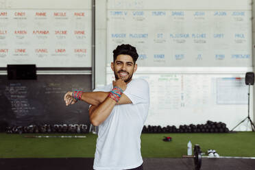 Young man smiling while stretching hand at gym - MARF00011