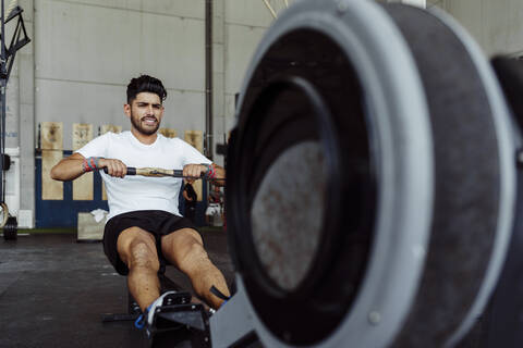 Sportler beim Training mit dem Rudergerät im Fitnessstudio, lizenzfreies Stockfoto