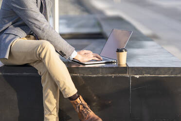 Geschäftsmann mit Kaffeetasse und Laptop auf einer Bank sitzend - GGGF00440