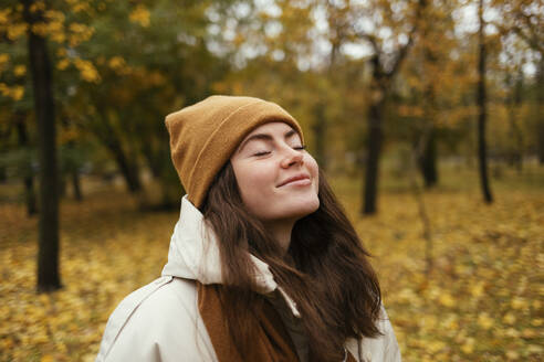 Lächelnde junge Frau mit geschlossenen Augen im herbstlichen Park - OYF00266