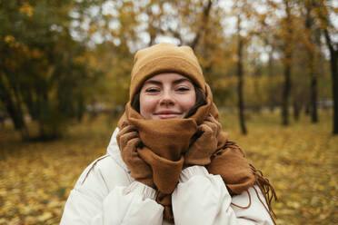 Smiling young woman wrapped up in scarf in autumn park - OYF00268
