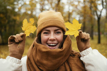 Fröhliche junge Frau mit Herbstblättern in einem öffentlichen Park - OYF00274
