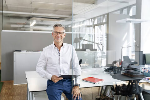 Glücklicher Geschäftsmann mit digitalem Tablet, das auf dem Schreibtisch im Büro liegt, lizenzfreies Stockfoto