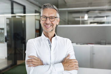 Happy male entrepreneur with arms crossed at work place - PESF02372