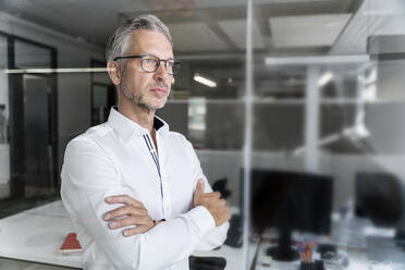 Confident male professional with arms crossed looking away in office - PESF02373