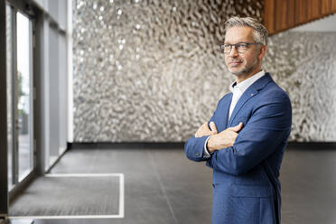 Confident businessman with arms crossed in office lobby - PESF02377