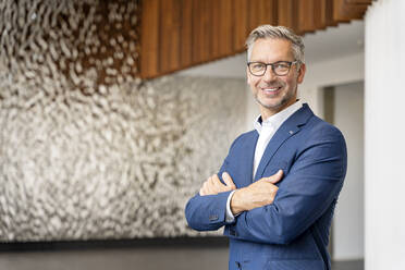 Smiling male entrepreneur with arms crossed in office lobby - PESF02378