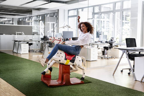 Fröhliche Unternehmerin auf Schaukelpferd im Büro - PESF02384