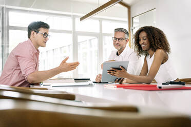 Eine lächelnde Geschäftsfrau zeigt ihren Kollegen während einer Besprechung im Büro ein digitales Tablet - PESF02388