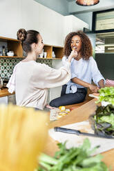 Geschäftsfrau füttert Mitarbeiterin mit Gemüse beim gemeinsamen Kochen in der Büroküche - PESF02393