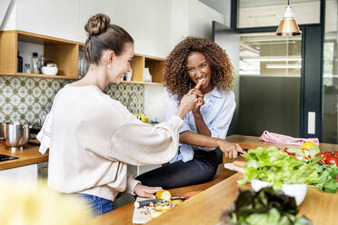 Geschäftsfrau isst Karotte von Kollege bei der Essenszubereitung in Büroküche - PESF02394