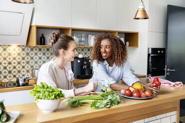 Smiling female coworkers looking at each other while leaning on counter in office kitchen - PESF02395