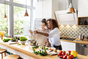 Female coworkers cooking spaghetti together at work place kitchen - PESF02399