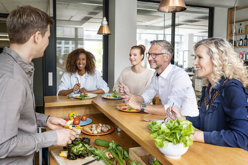 Lächelnde Geschäftsleute mit Essen auf der Küchentheke im Büro - PESF02407