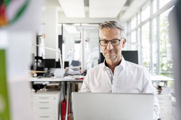 Lächelnder Geschäftsmann bei der Arbeit am Laptop im Büro - PESF02416