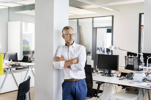 Confident businessman with arms crossed leaning on column in office stock photo