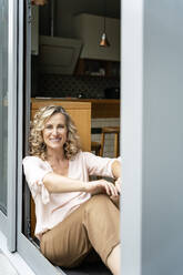 Happy female entrepreneur sitting at doorway of office cafeteria - PESF02449