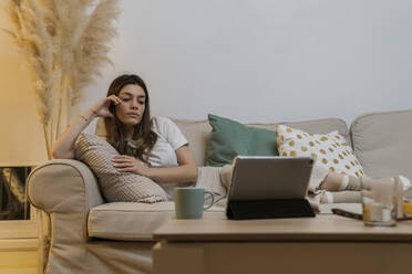 Junge Frau mit digitalem Tablet entspannt sich auf dem Sofa zu Hause - MTBF00774
