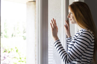 Frau schaut durch ein Fenster, während sie zu Hause steht - AFVF07784