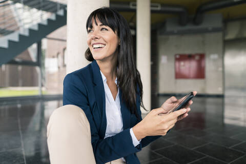 Smiling businesswoman looking away while holding smart phone in office stock photo