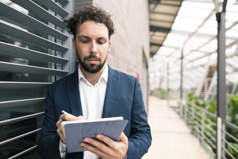Männlicher Unternehmer, der ein digitales Tablet benutzt, während er im Flur eines Büros steht - JOSEF02530