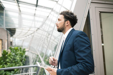 Businessman with digital tablet looking away in office - JOSEF02531