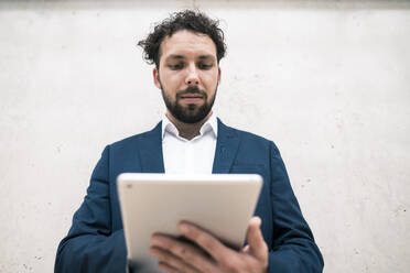 Männlicher Unternehmer mit digitalem Tablet an der Wand im Büro - JOSEF02532