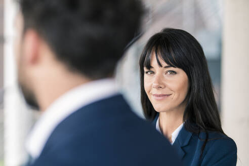 Lächelnde Unternehmerin im Gespräch mit einem männlichen Kollegen während einer Bürobesprechung - JOSEF02557