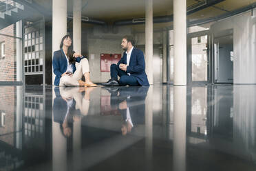 Professionelle männliche und weibliche Kollegen diskutieren, während sie in der Lobby im Büro sitzen - JOSEF02559